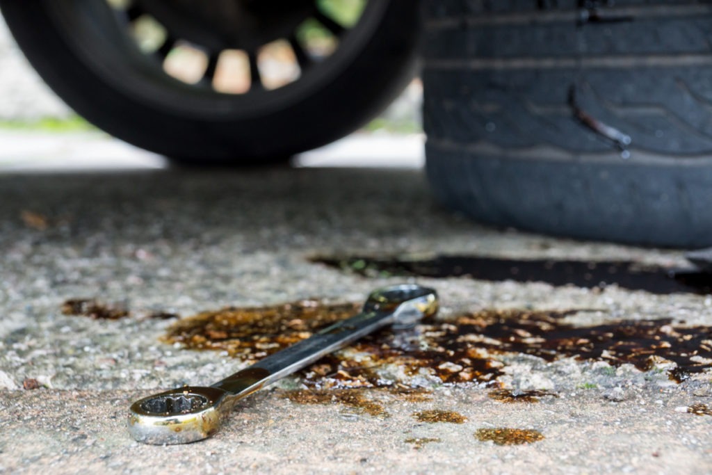 A socket wrench left on the floor in a puddle of oil showing signs of vehicle repair work