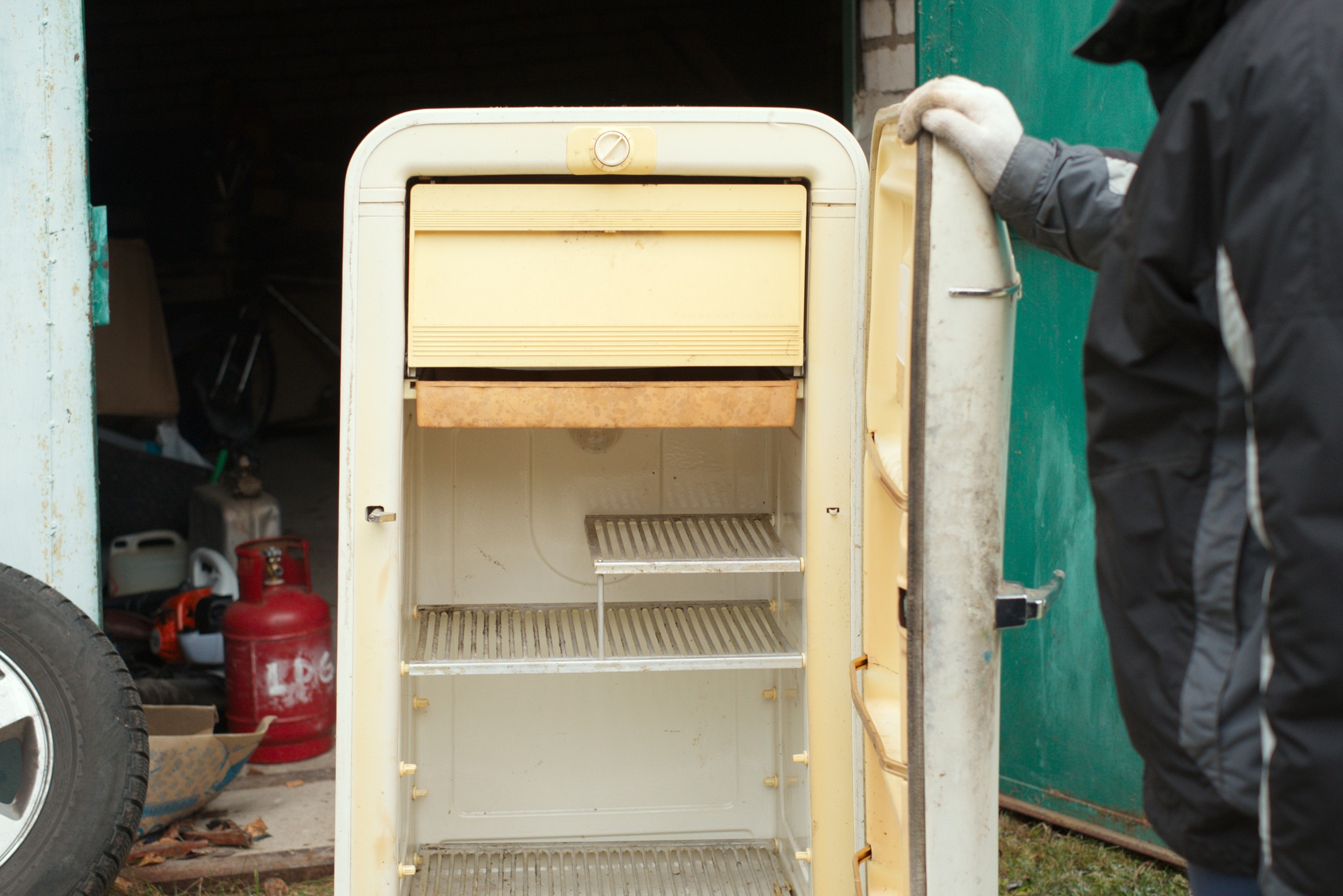 A man about to discard old fridge standing next to the open garage door, outdoor cropped shot