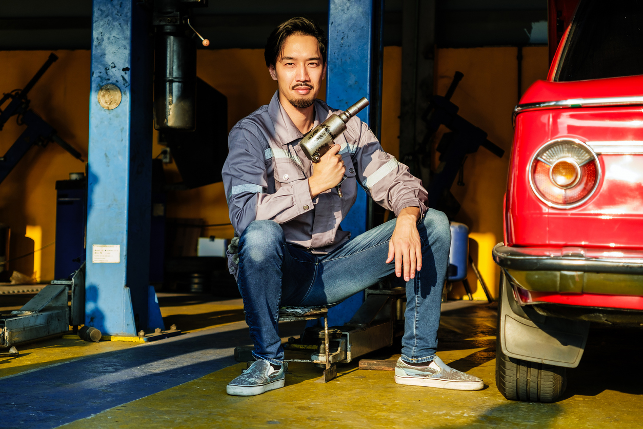 a mechanic posing with a tool, with a vintage car in the background