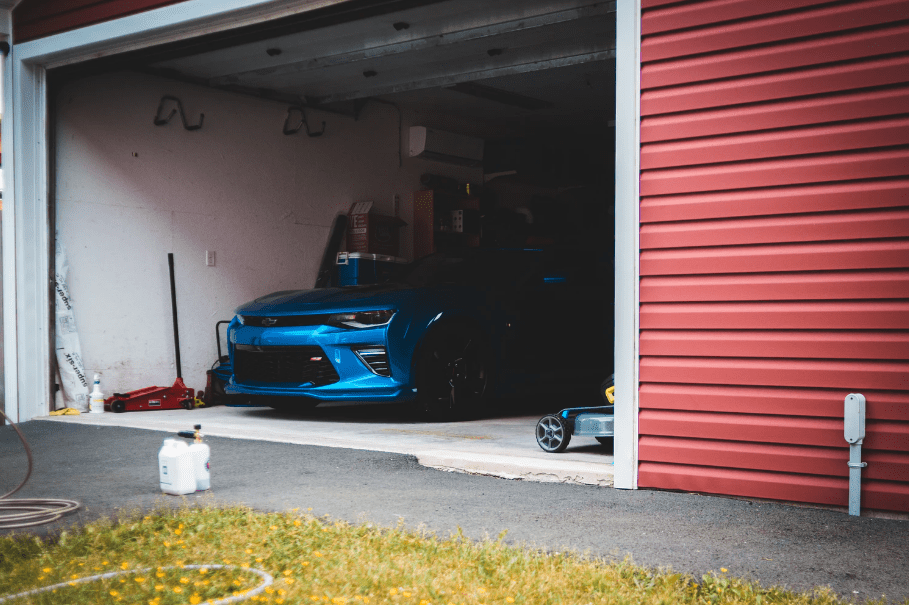 An image of an open garage door housing tools and a blue Chevrolet Camaro.