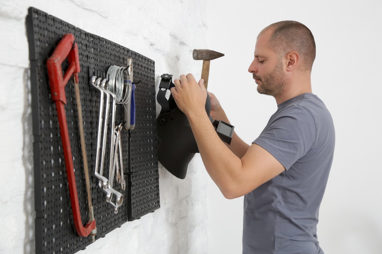 Man organizing his tools on the plastic pegboard on the wall in workshop