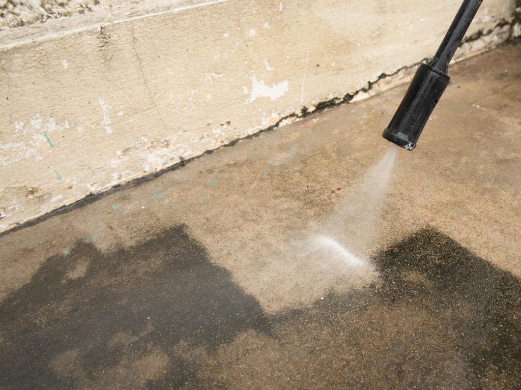 Worker cleaning dirt outdoor floor with high pressure water jet